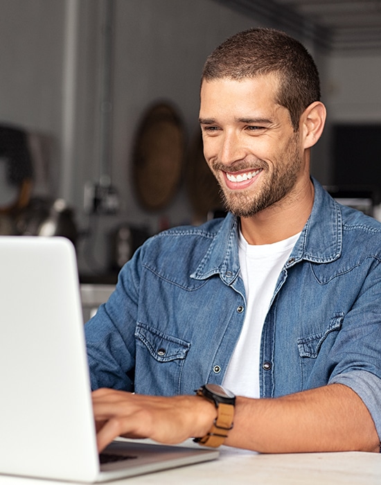 Hombre joven y sonriente utilizando un portátil en casa