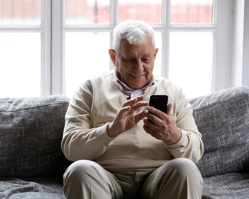 Hombre de avanzada edad sonriente mientras utiliza su teléfono móvil