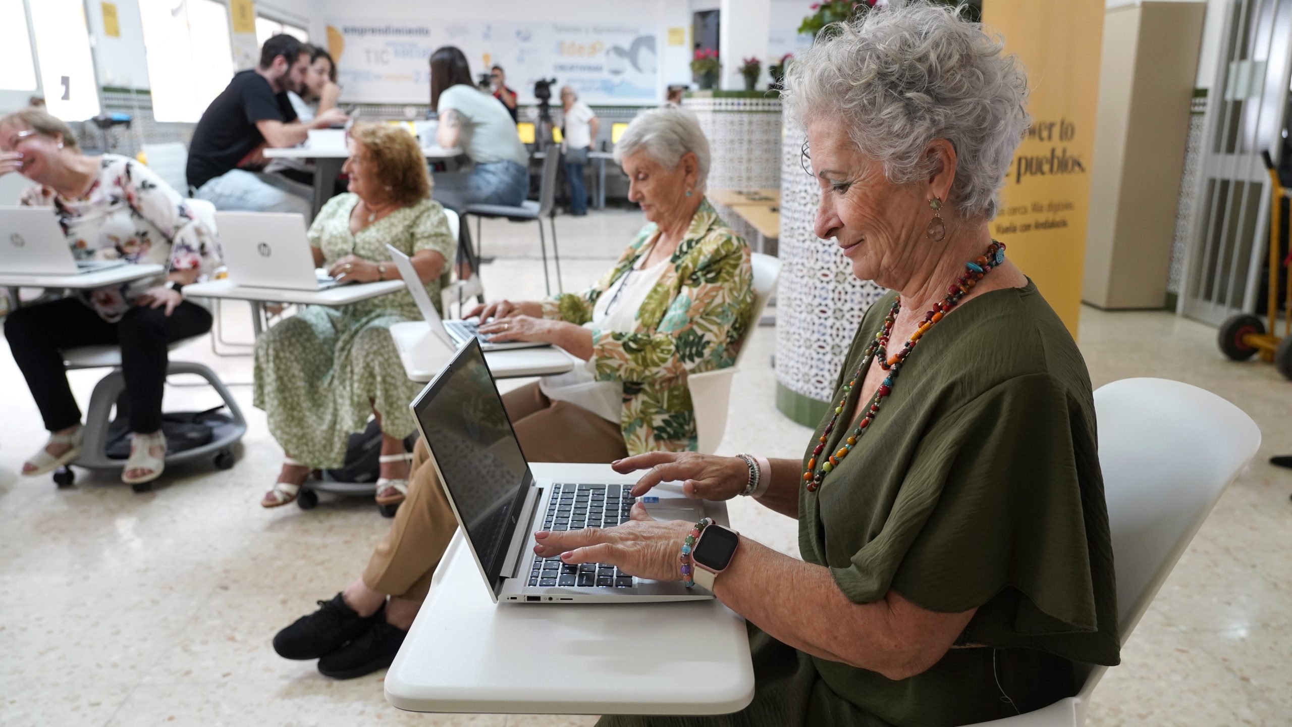 Personas mayores integrándose en la era digital mediante el uso de ordenadores portátiles en un espacio de aprendizaje dinámico.