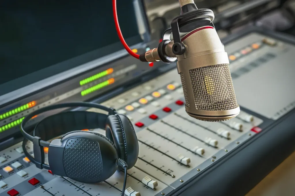 Micrófono de estudio y auriculares sobre una mesa de mezclas de audio en un entorno de grabación.