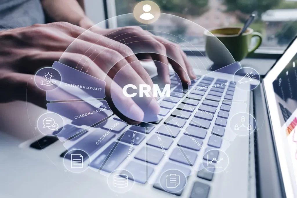 Manos escribiendo en un ordenador portátil con una interfaz gráfica de CRM superpuesta que muestra funciones de gestión de clientes, comunicación y análisis de datos.