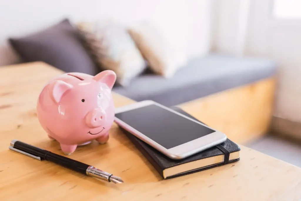 Hucha, móvil y cuaderno sobre una mesa de madera